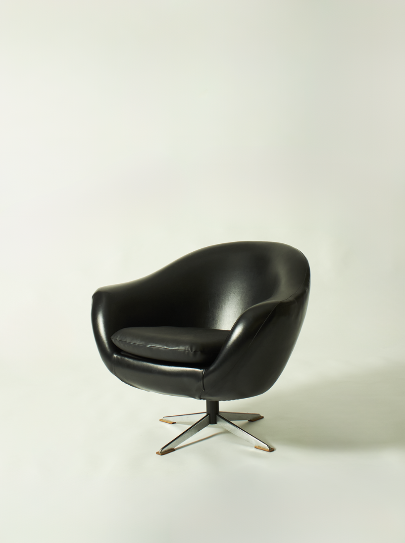 A black modern leather lounge chair with a rounded back and armrests, supported by a four-legged metal base, placed on a plain white background.