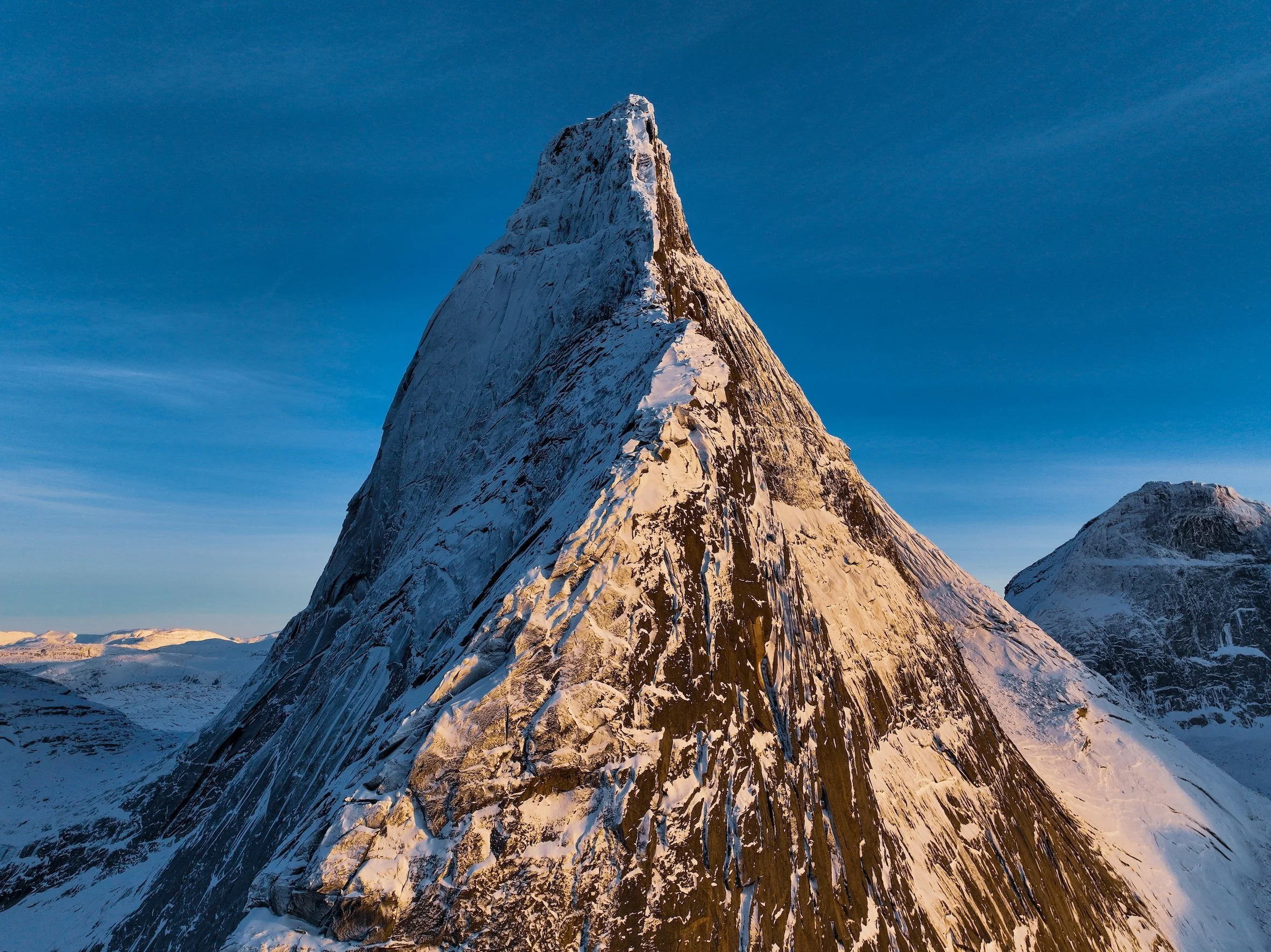 Berggipfel im Schnee bei Sonnenuntergang gegen blauen Himmel.