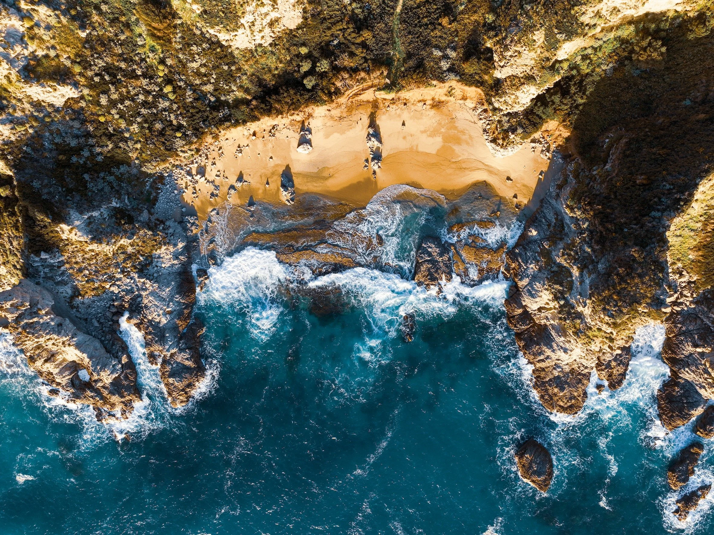Brechende Wellen an Klippen mit Strandstück