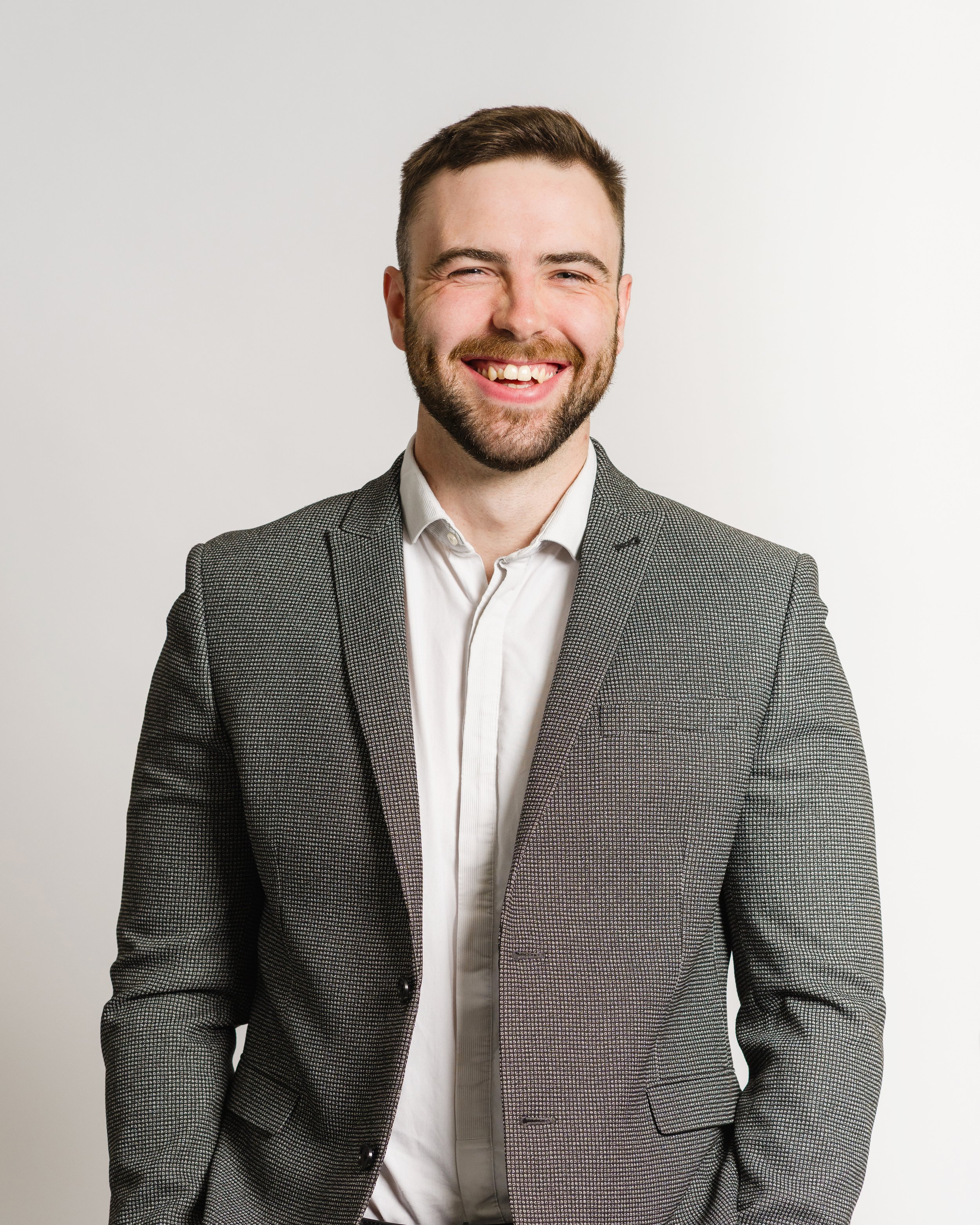 Headshot of smiling man in a checkered blazer and white shirt against a plain background.