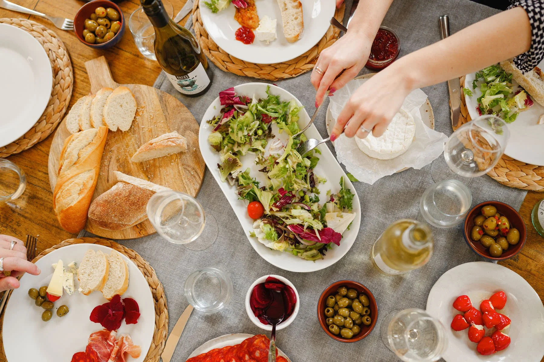 A top-down view of a table set for a meal with various dishes, including a salad, bread, olives, cheese, tomatoes, and wine.