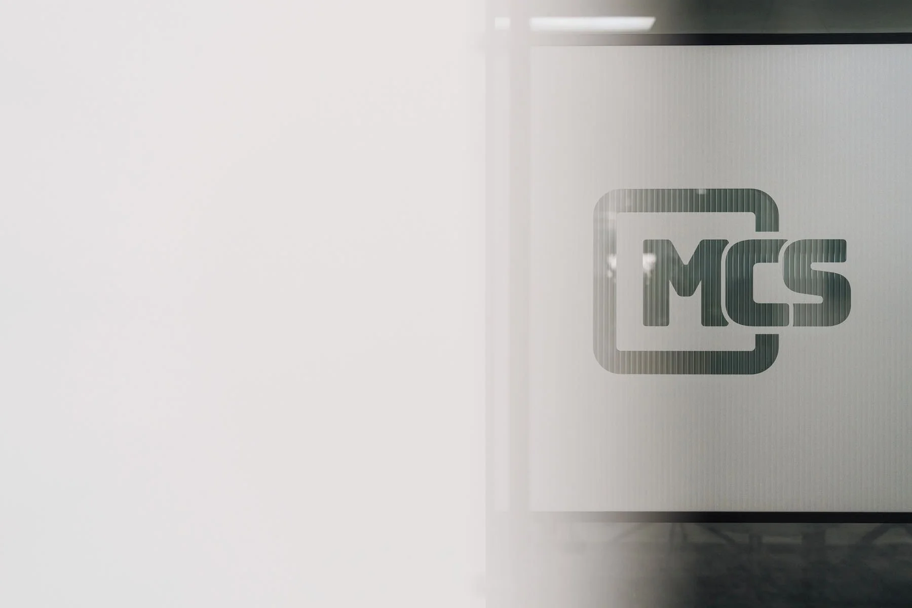 A logo on a glass surface features the letters 'MCS' inside a rounded rectangle outline.