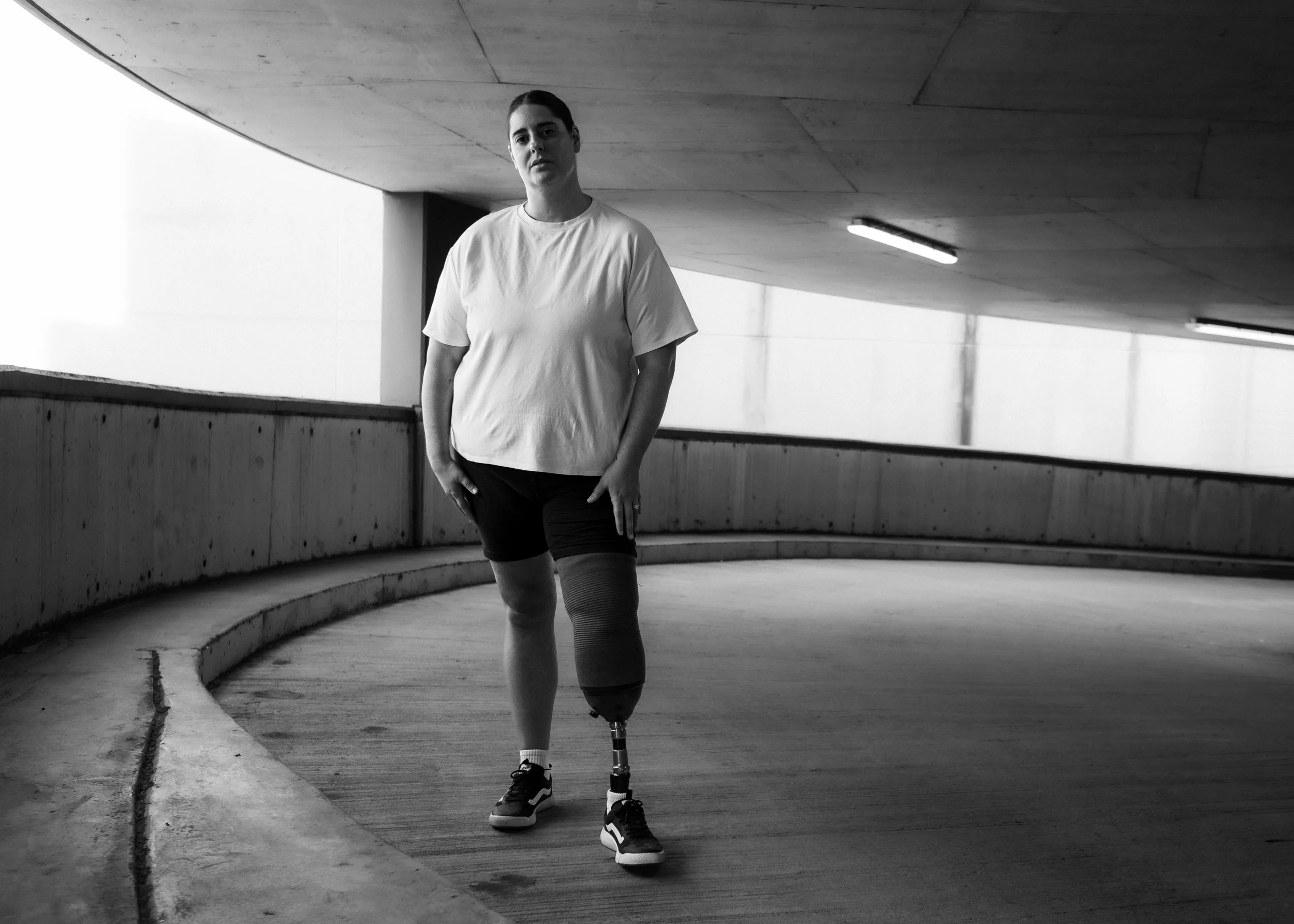 A woman with an artificial leg walking on a curved ramp in an underground parking garage.