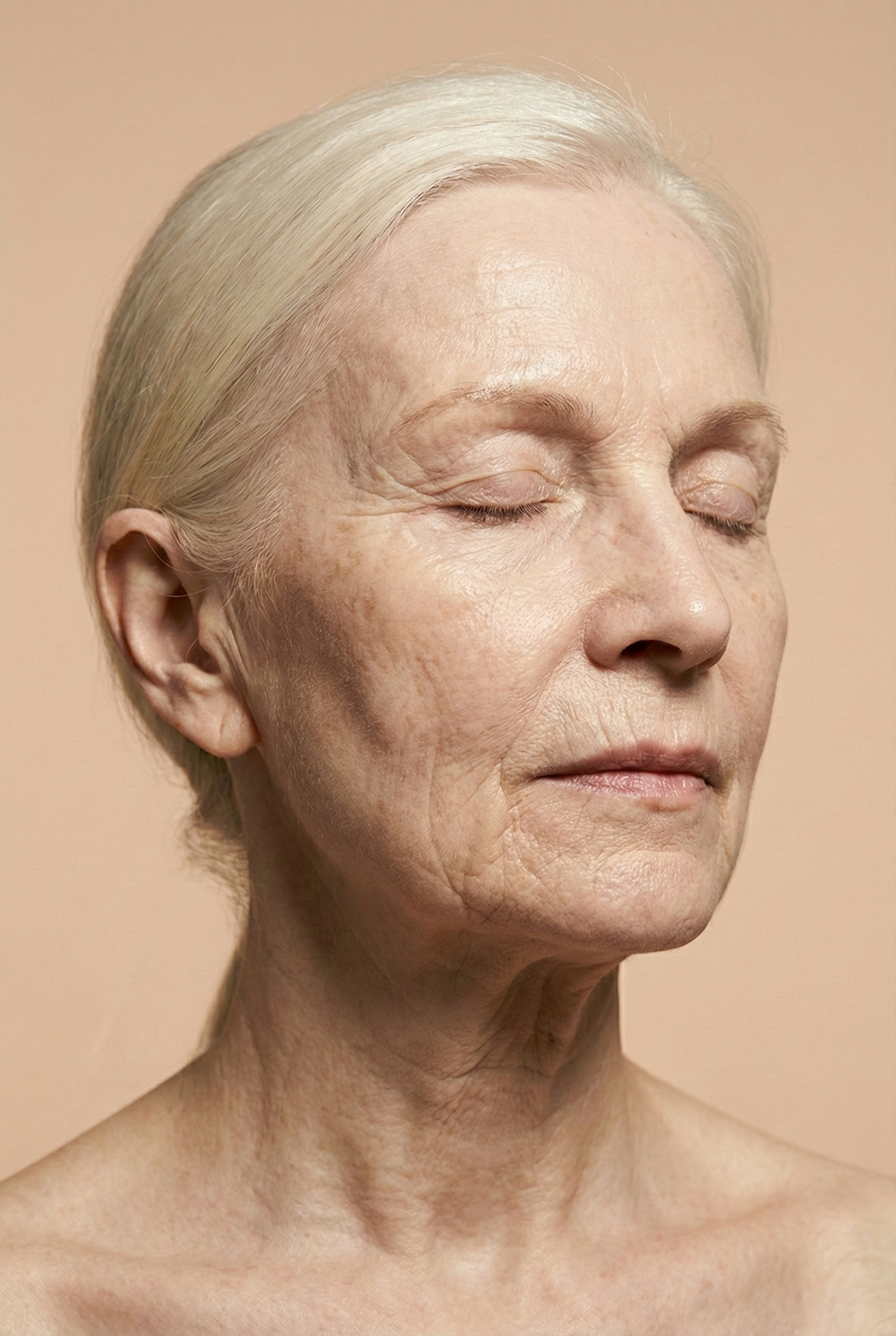Close-up of an elderly woman with closed eyes, light skin, and short, platinum blonde hair. Her face shows signs of aging with wrinkles and age spots, against a neutral beige background.