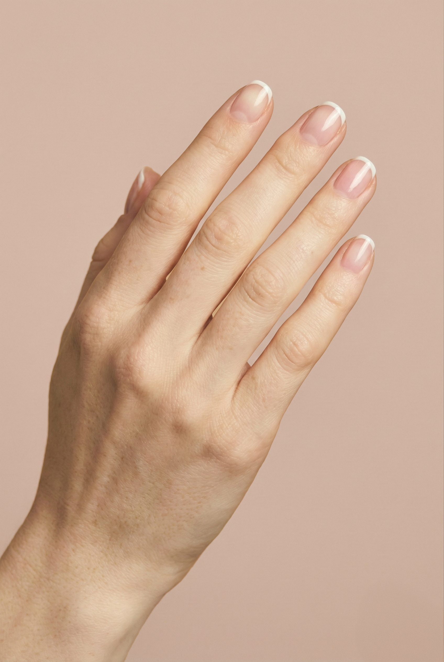 Close-up of a human hand with well-manicured nails against a light pink background.