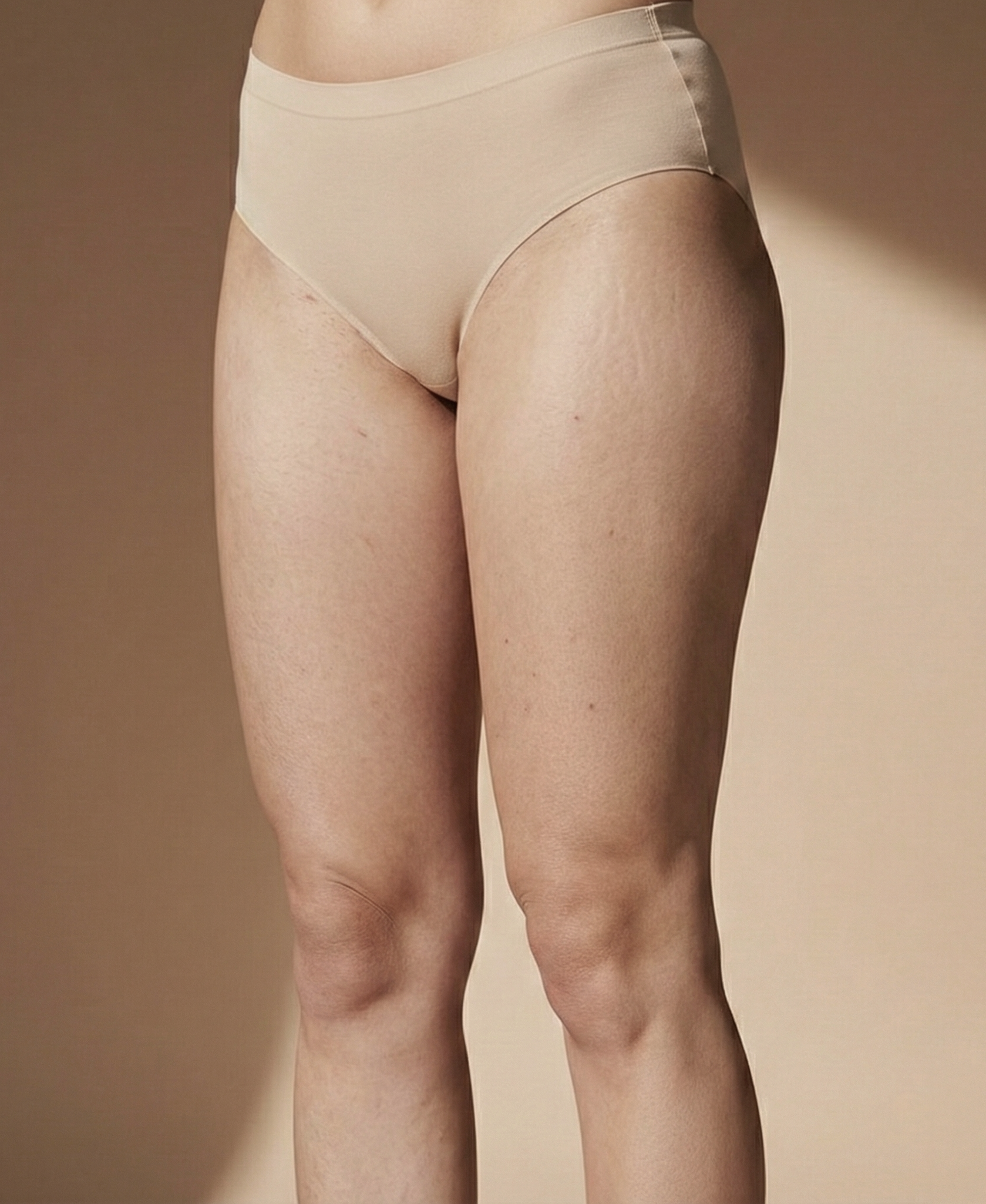 Close-up of a person's lower body wearing beige high-waisted underwear, with background in a neutral tone.