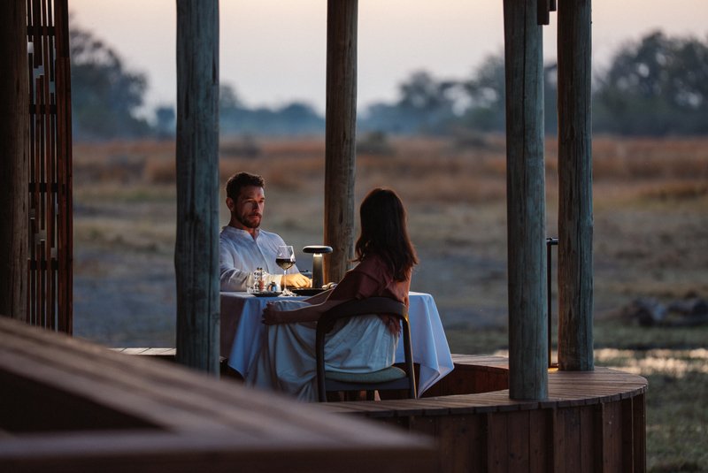 Young couple sipping red wine before dinner at a private table for two on a balcony overlooking the African savannah