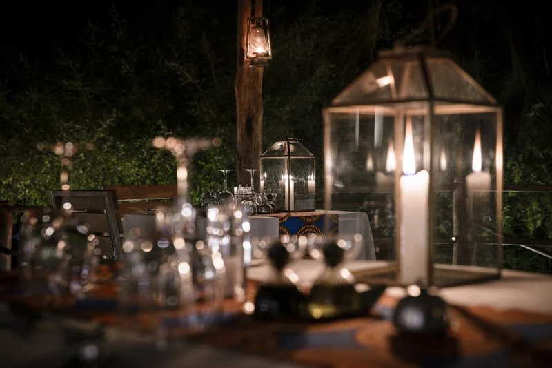 Close-up of a candle reflecting light on polished glassware on a table set for a private dinner for two on an African safari