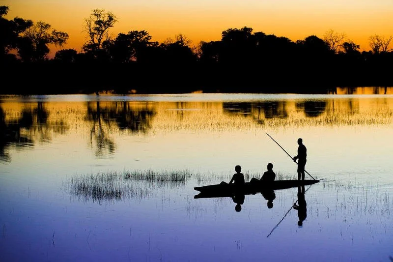 Evening silhouette of two guests being poled on a mokoro ride in the Okavango Delta, Botswana
