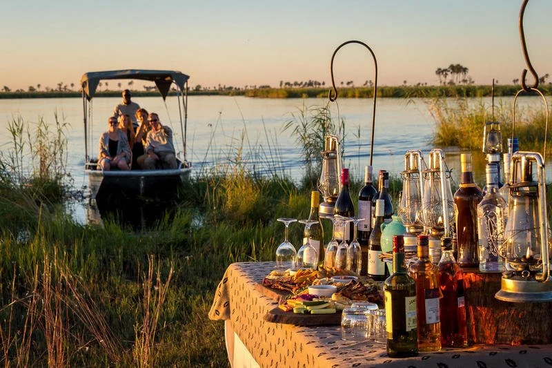 Guests arriving by boat from an afternoon African river activity to a surprise sundowner setup on the shoreline