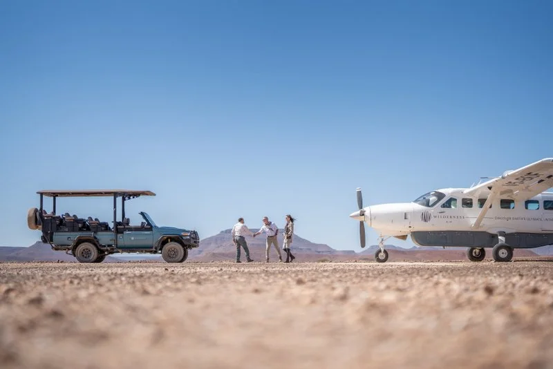 Guide greeting guests on a sandy airstrip in front of a light aircraft