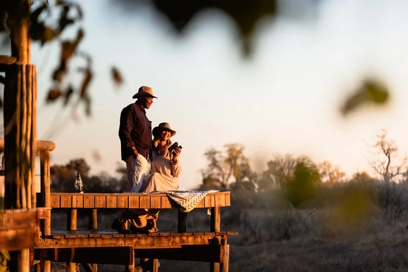 Couple on their lodge room private deck gazing out at the African savannah at sunset