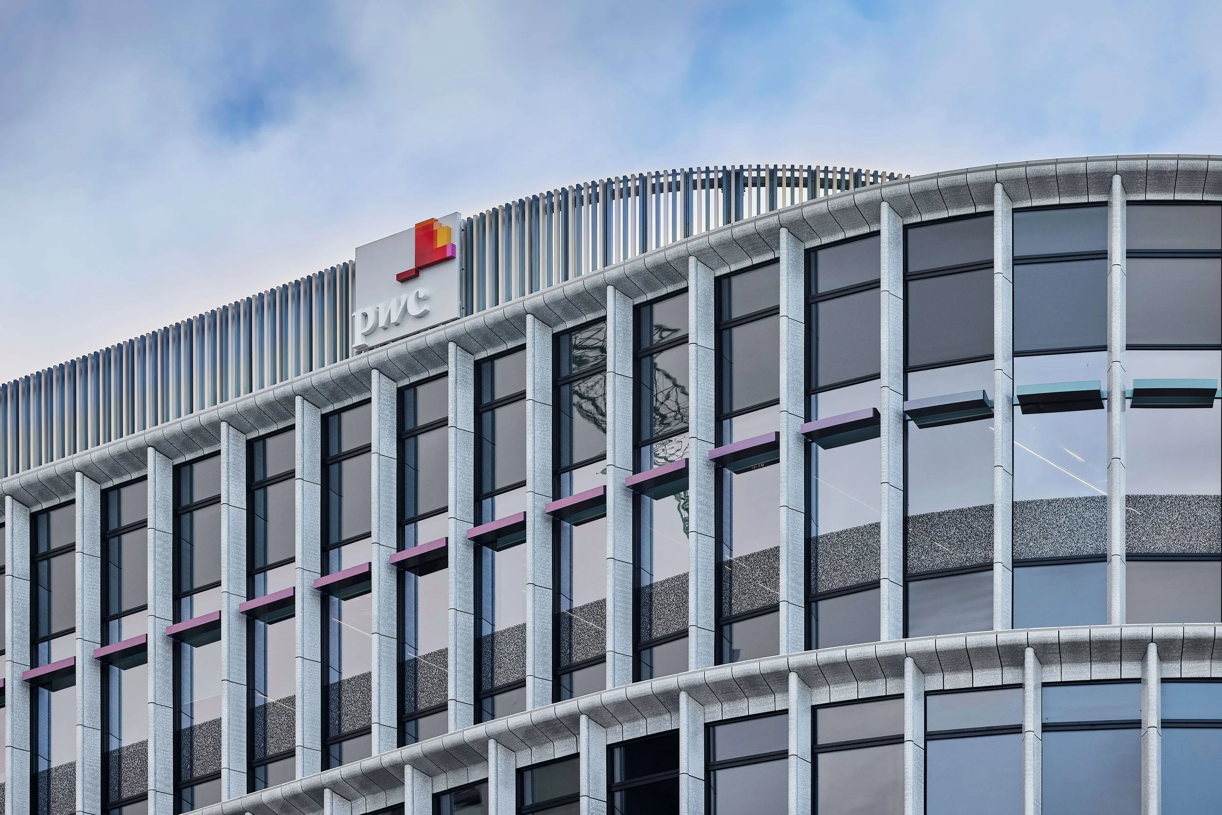 Exterior of a modern office building with the PwC logo at the top, glass windows, and metal architectural accents.