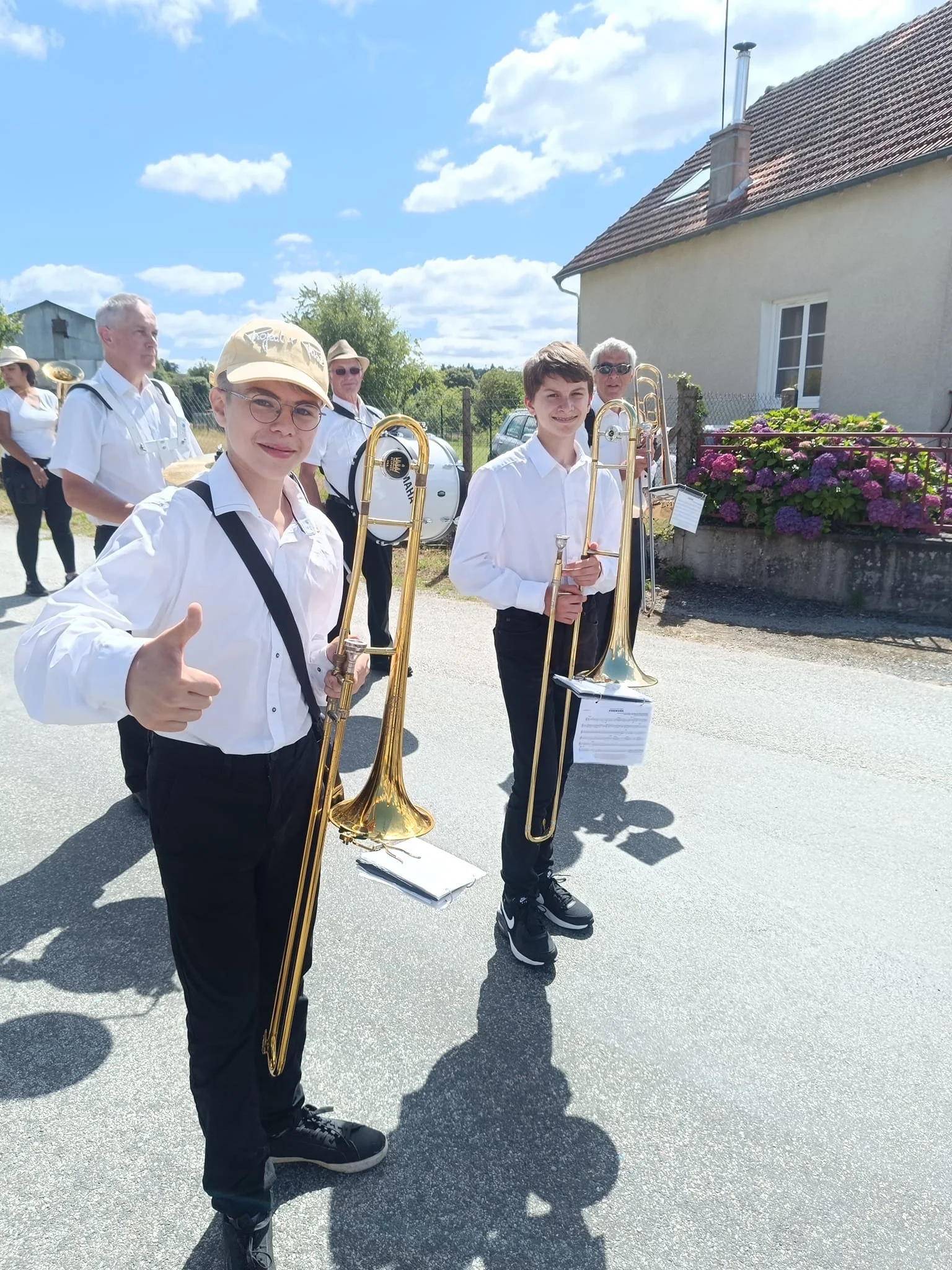 Jeunes musiciens avec trombones, habillés en blanc, lors d'une parade en plein air sous un ciel ensoleillé