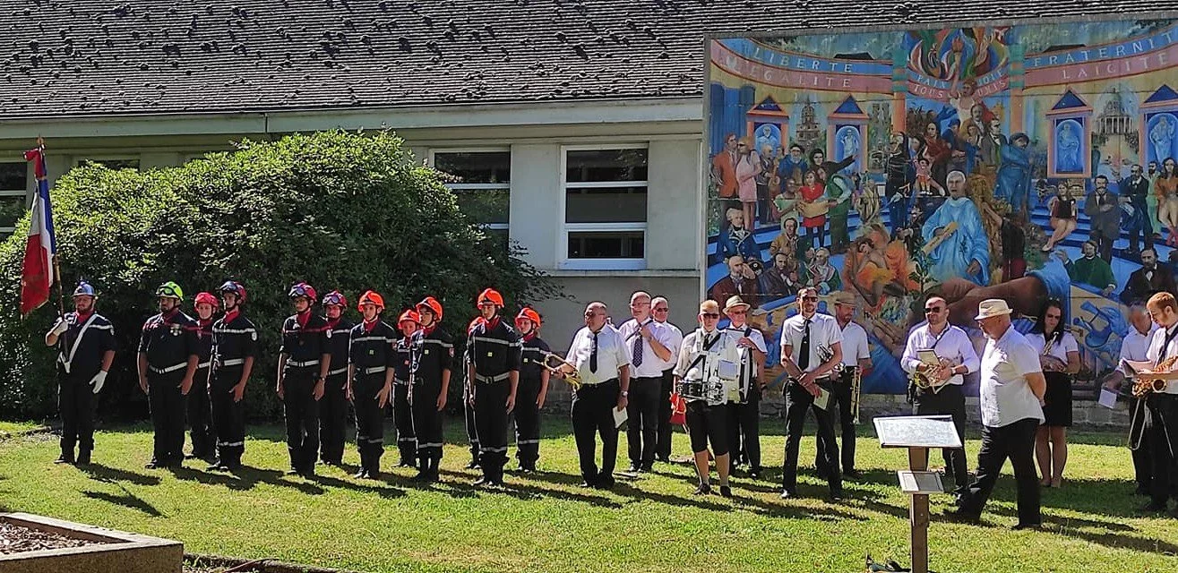 Un groupe de personnes avec un uniforme de pompiers, certains portant un casque rouge, d'autres un casque jaune, en ligne devant un mur avec une grande fresque colorée.