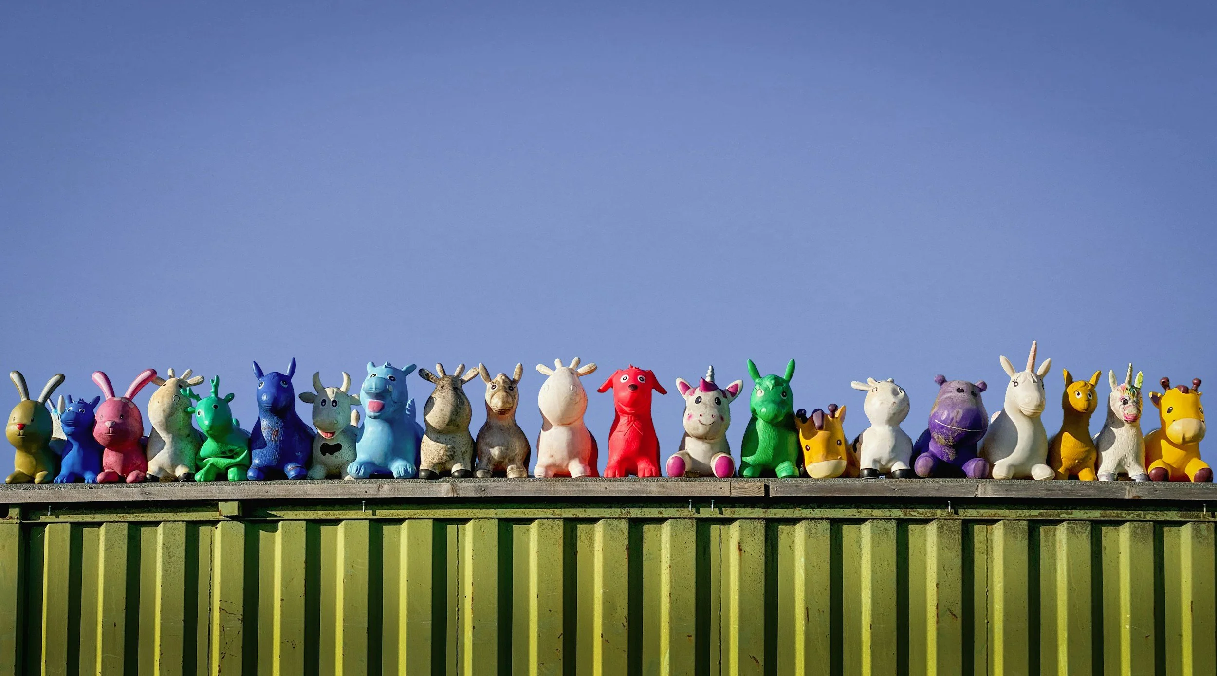A row of colorful, cartoonish animal figurines on a green surface against a blue sky.