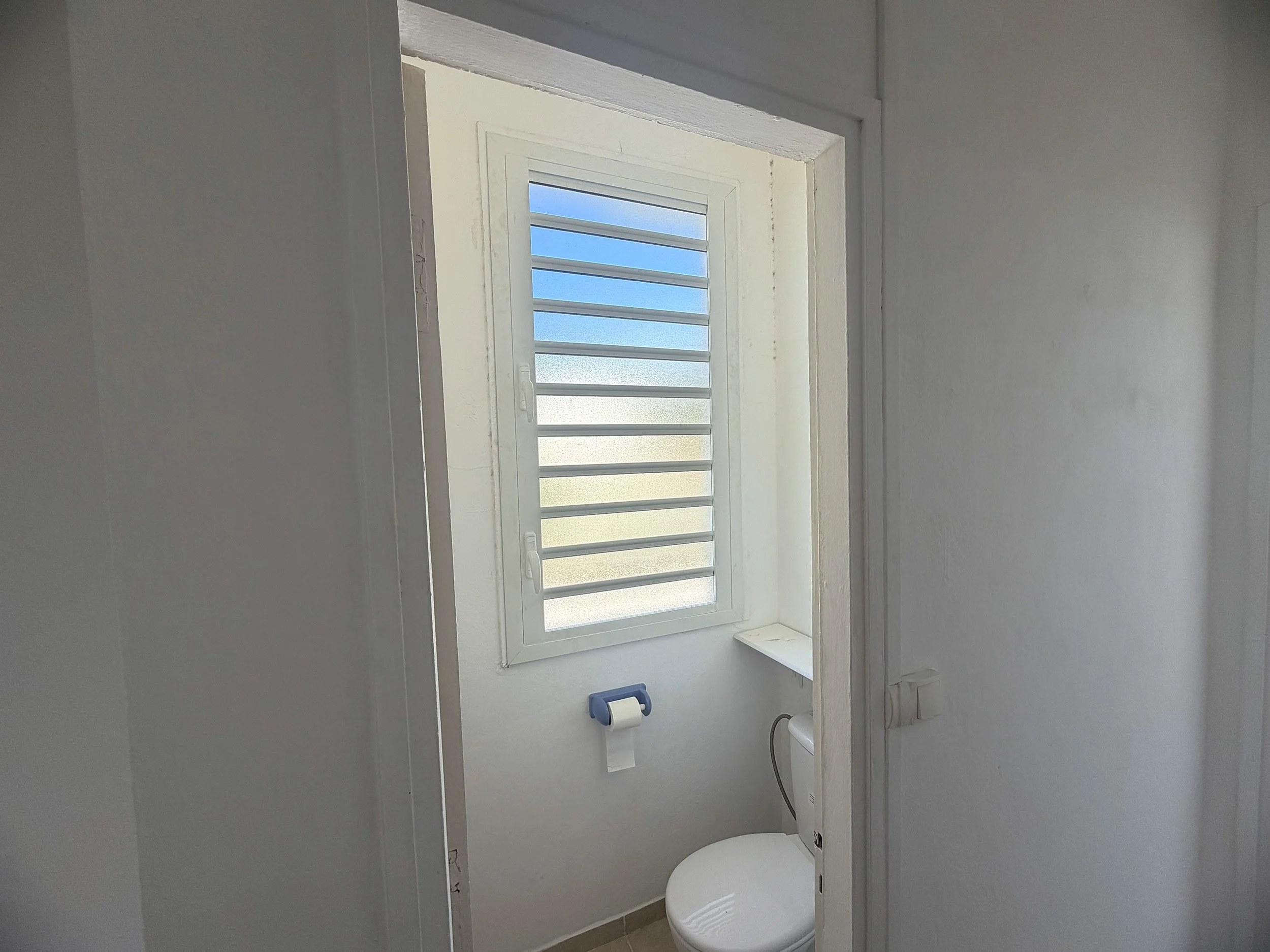Small bathroom with a toilet, a window with louvered glass panes, and white walls.
