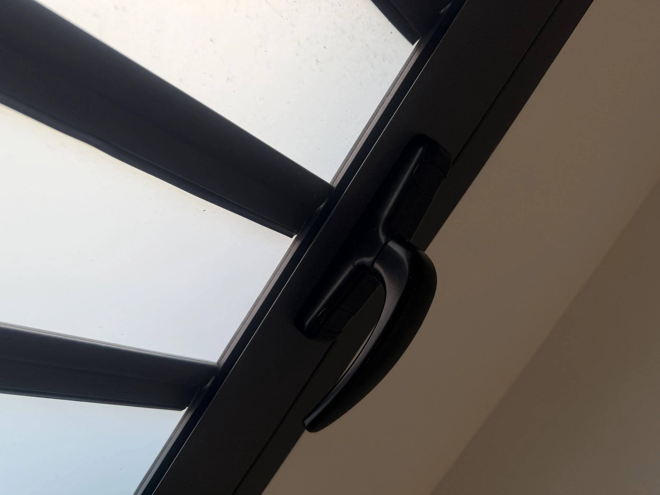 Close-up of a black window handle on a glass door, with a view of a clear sky through the window.