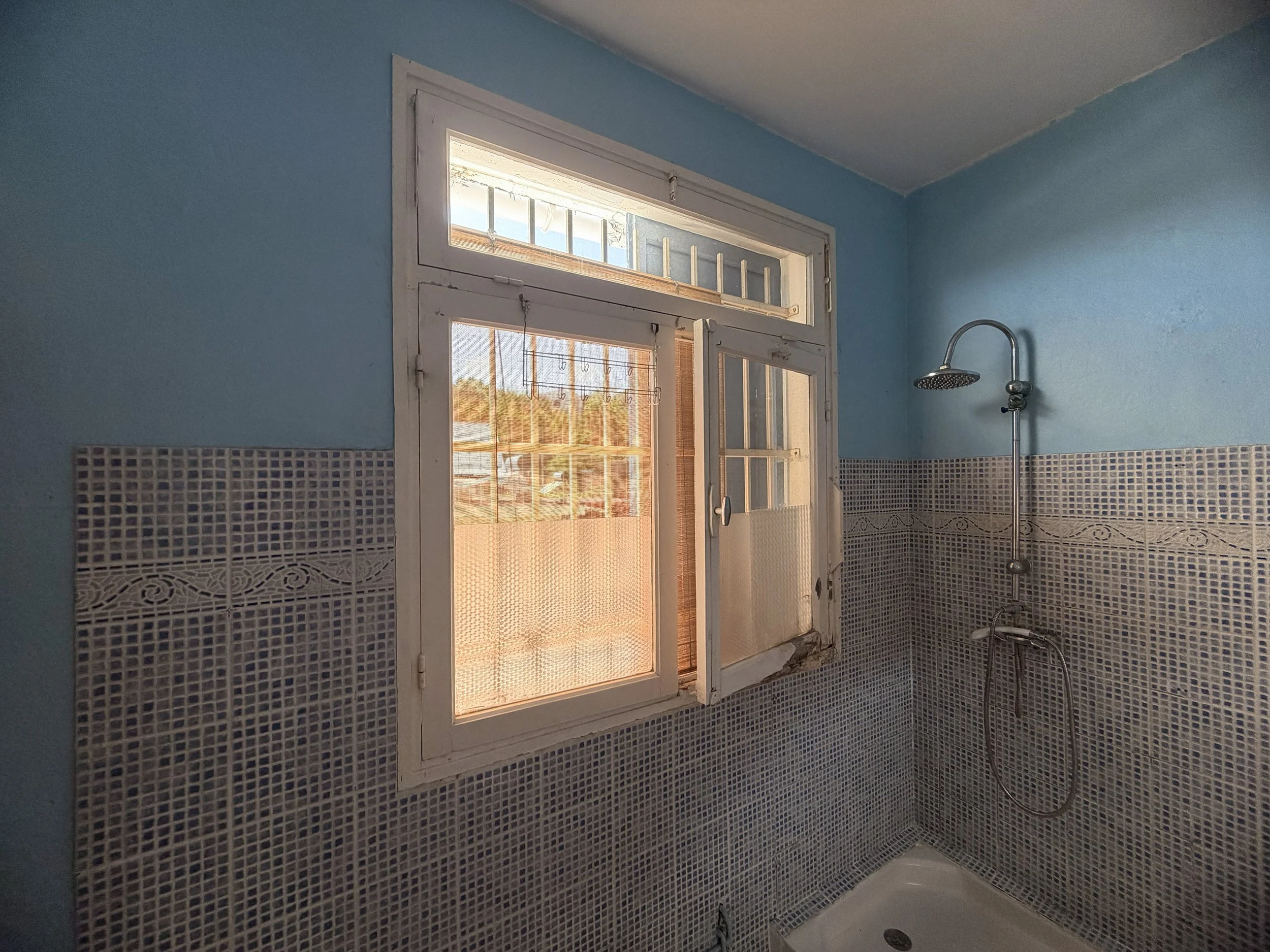 Bathroom with blue walls, a window with bars, mosaic tile walls, and a showerhead