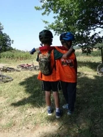 Two young children with their arms around each other and their backs to the camera looking out towards hills