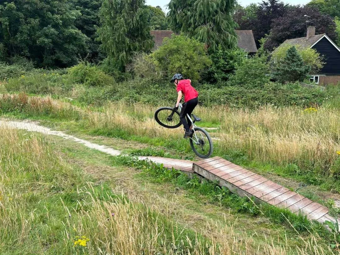 A person riding a BMX bike on a small wooden ramp in a grassy outdoor area.