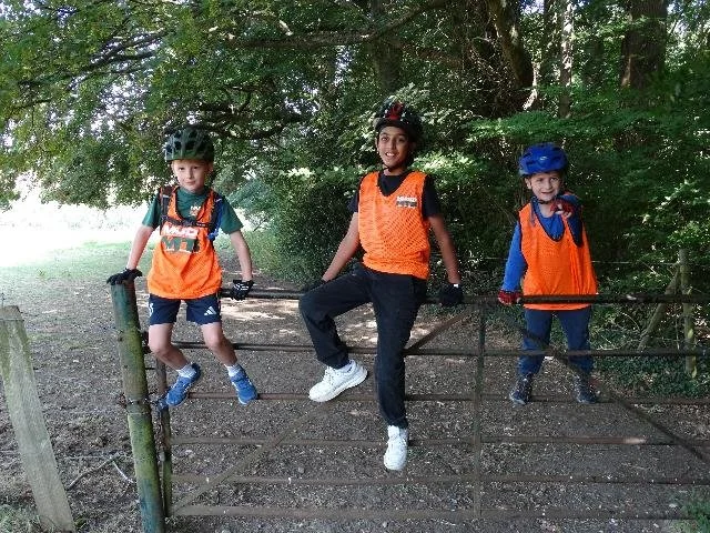 Group of children on a farm fence wearing Muddy MTB tops and helmets