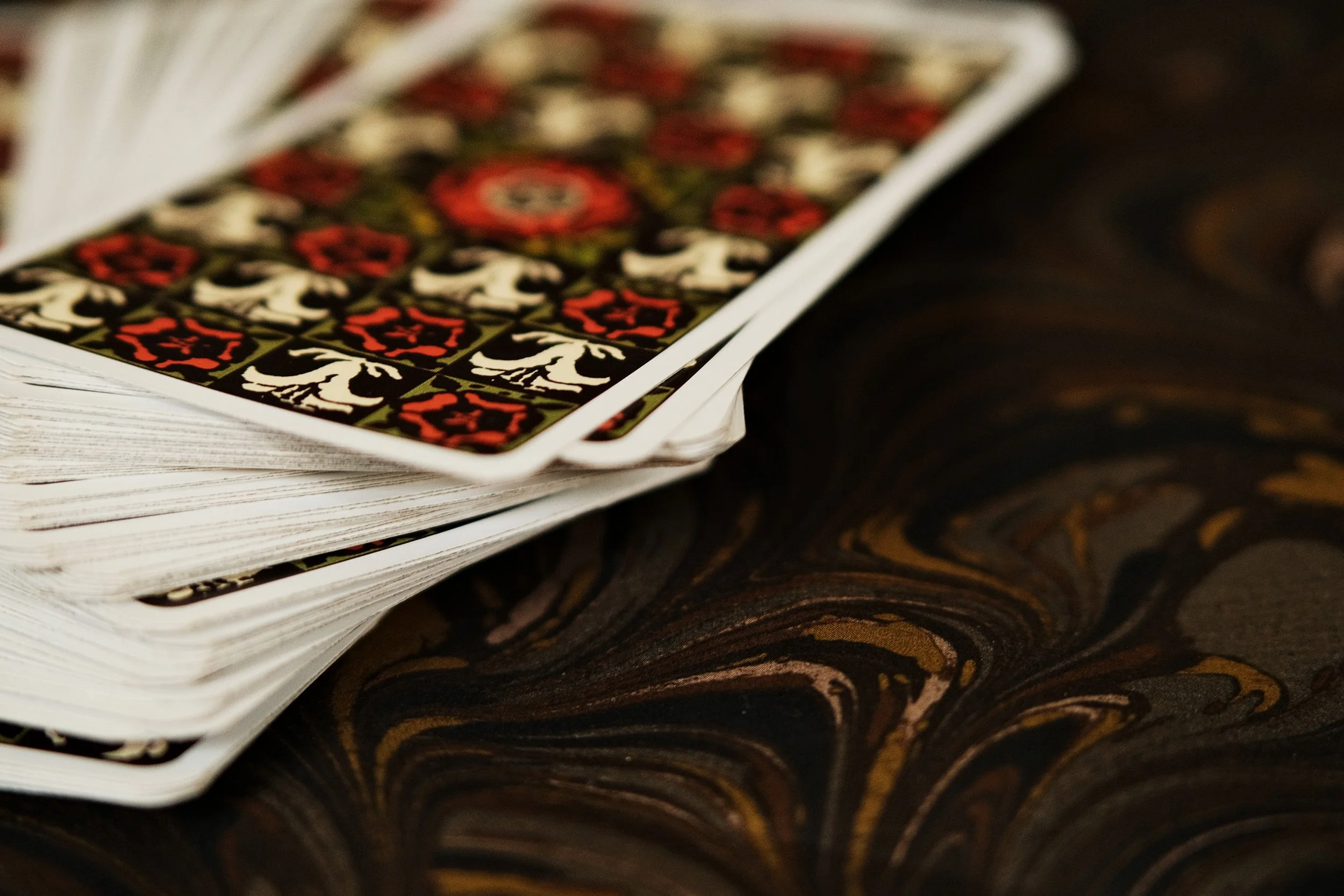 Close-up view of a deck of tarot cards, partially fanned out, showing the patterned back design with red, black, and white colors, resting on a dark, marbled fabric.