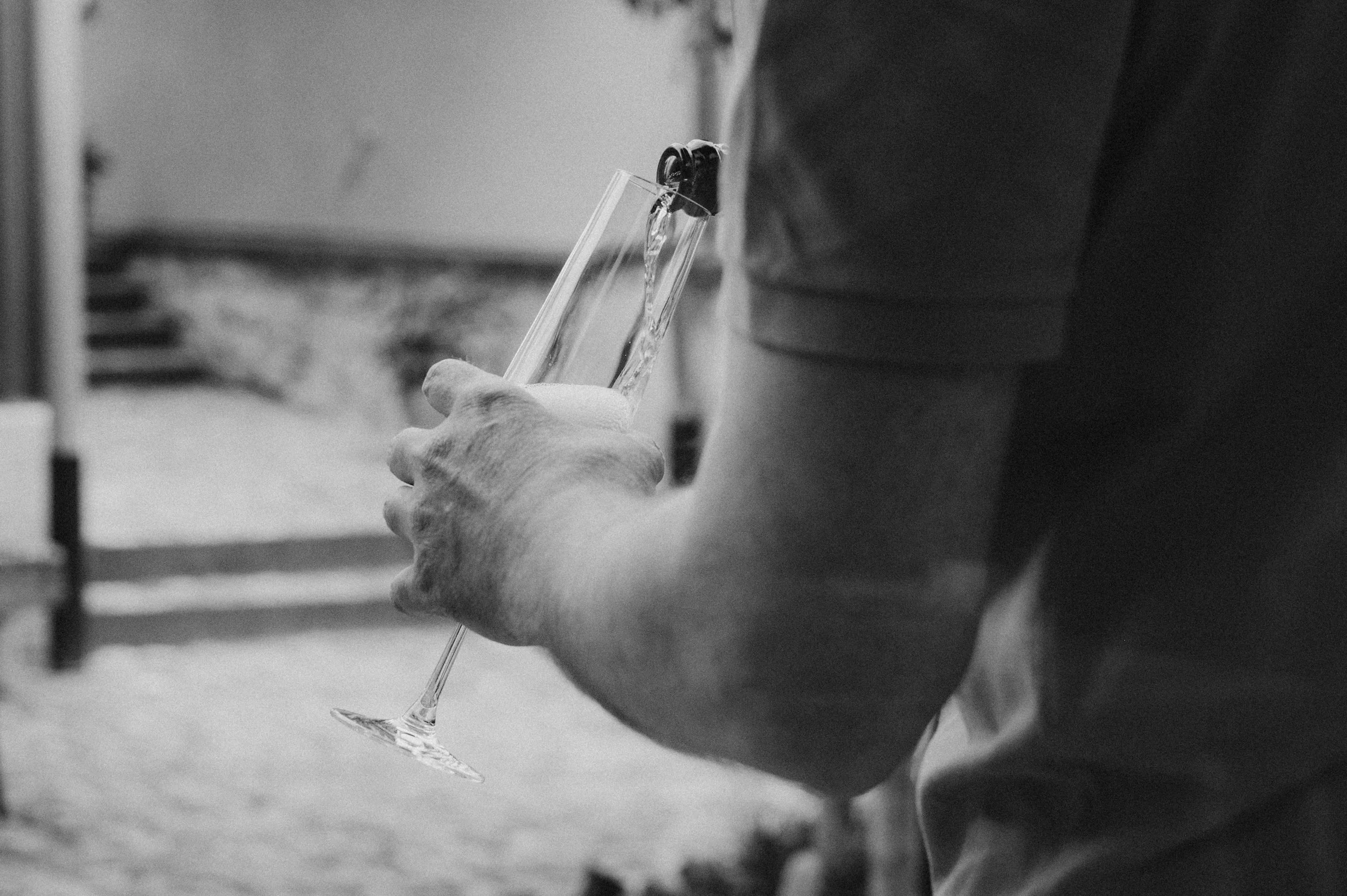 Nahaufnahme einer Person, die ein leeres Champagnerglas hält, in Schwarz-Weiß.