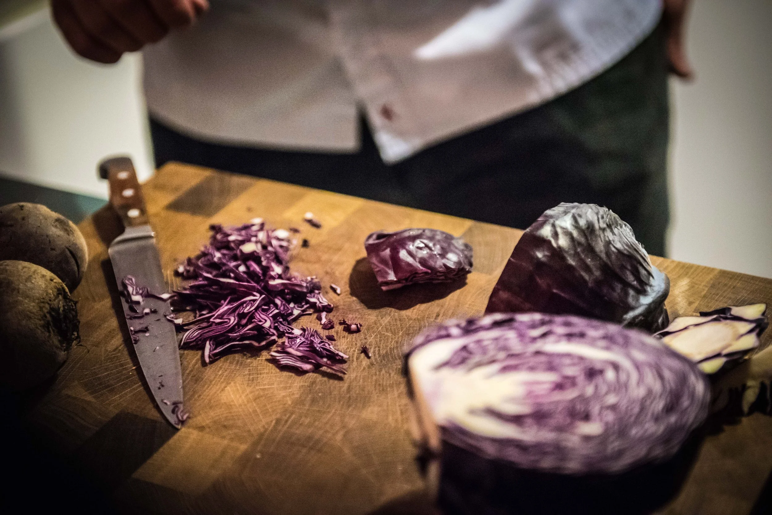 Schnittbretter mit geschnittenem roten Kohl, noch ungeschnittenes Garnelen- oder Radicchio-Kopf und rohe Rote Bete, daneben ein Messer auf einem Holztisch.