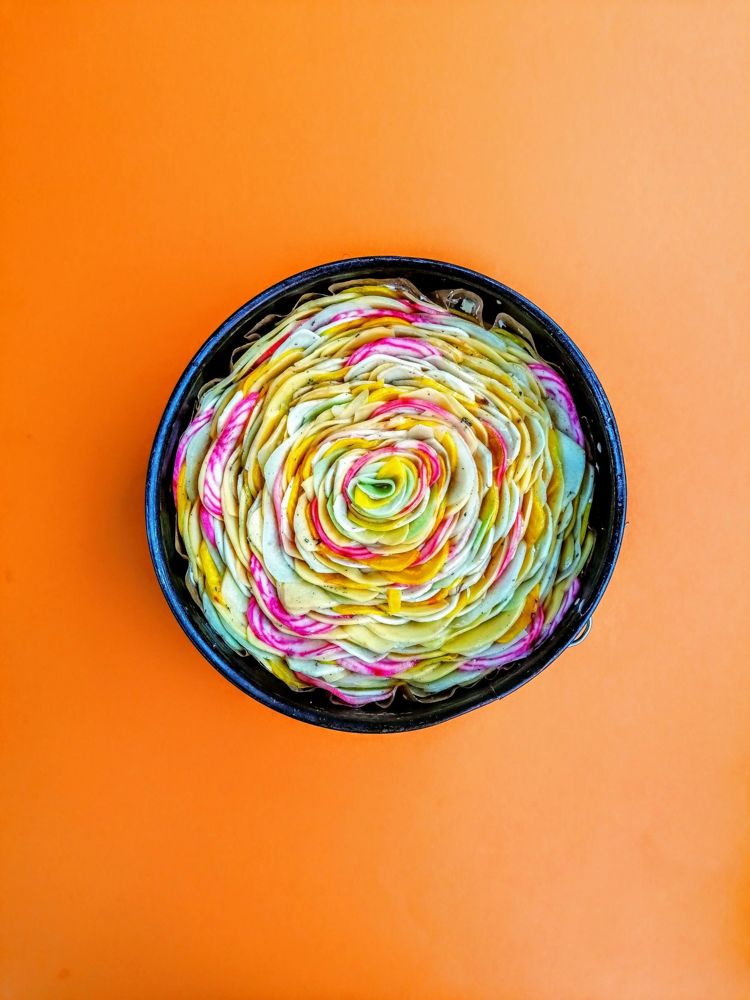 Buntes, spiralförmiges Gemüsegericht auf einem orangefarbenen Hintergrund.