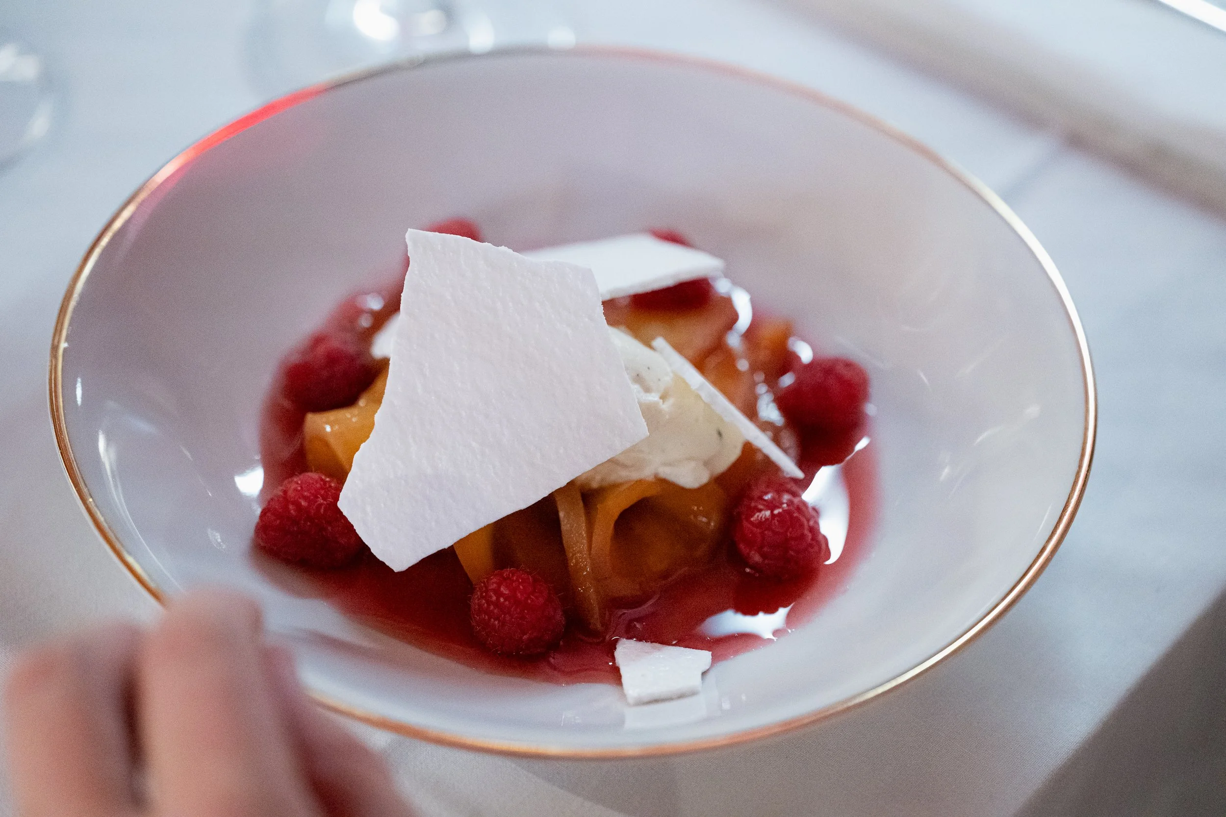Ein Dessert mit Baiser, Himbeeren und Pfirsich in einer weißen Schale mit Goldrand.