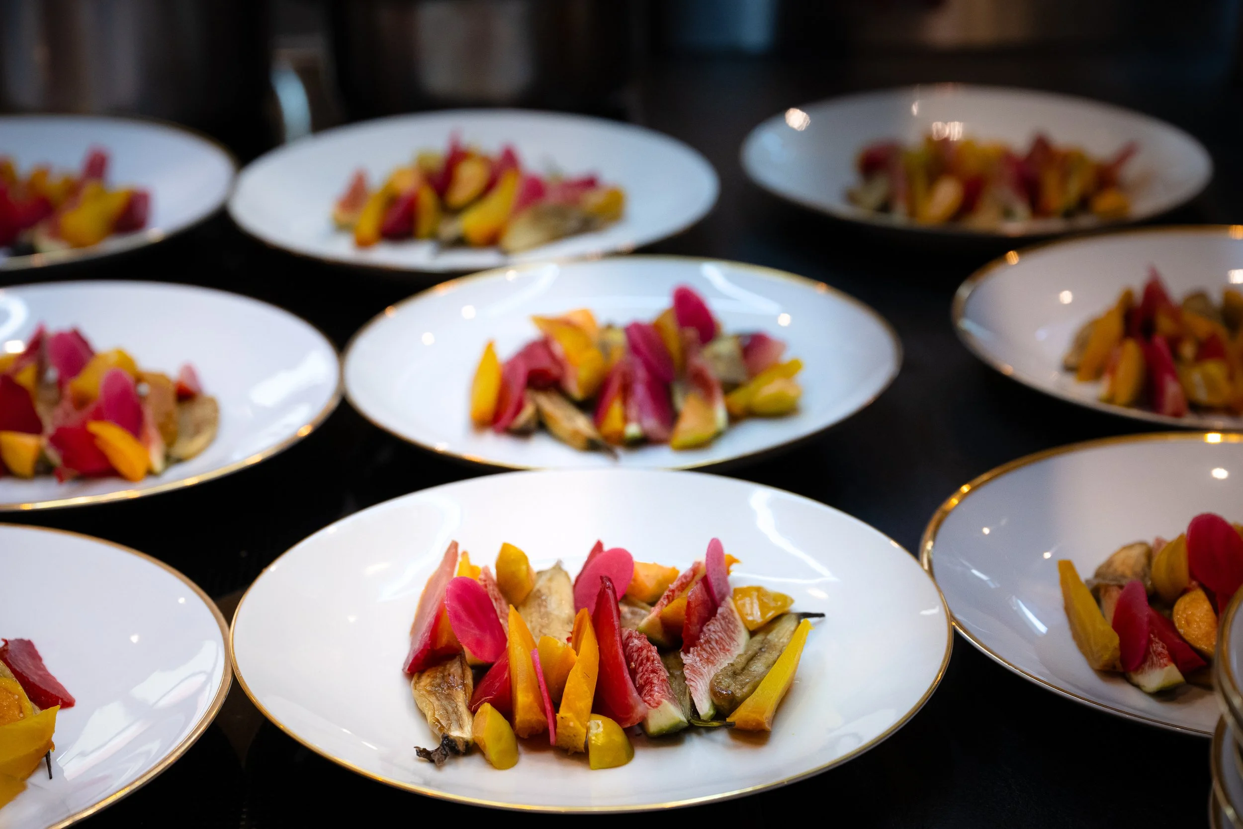 Mehrere weiße Teller mit schön angerichtetem Gemüse auf einem dunklen Tisch.