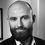 Et svart-hvitt portrett av en person med skjegg og skjorte, som smiler litt.