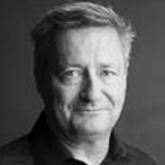 Bilde av en eldre mann med grått hår, iført svart t-skjorte, mot en mørk bakgrunn.