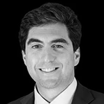 Et svart-hvitt bilde av en smilende mann med mørkt, krøllet hår i formell dress.