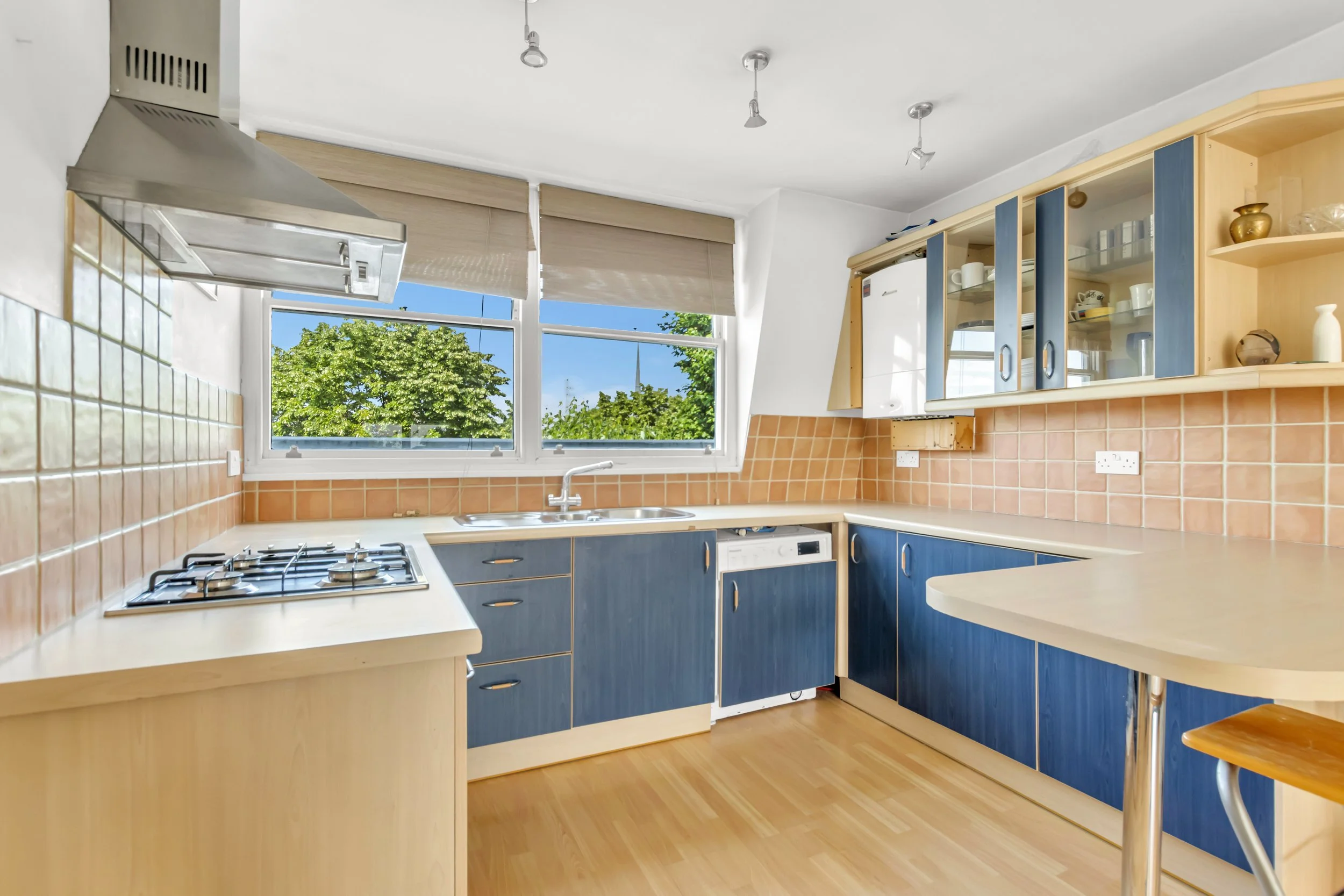 Kitchen with blue and wood cabinets, beige countertops, a window showing green trees outside, and a gas stove.