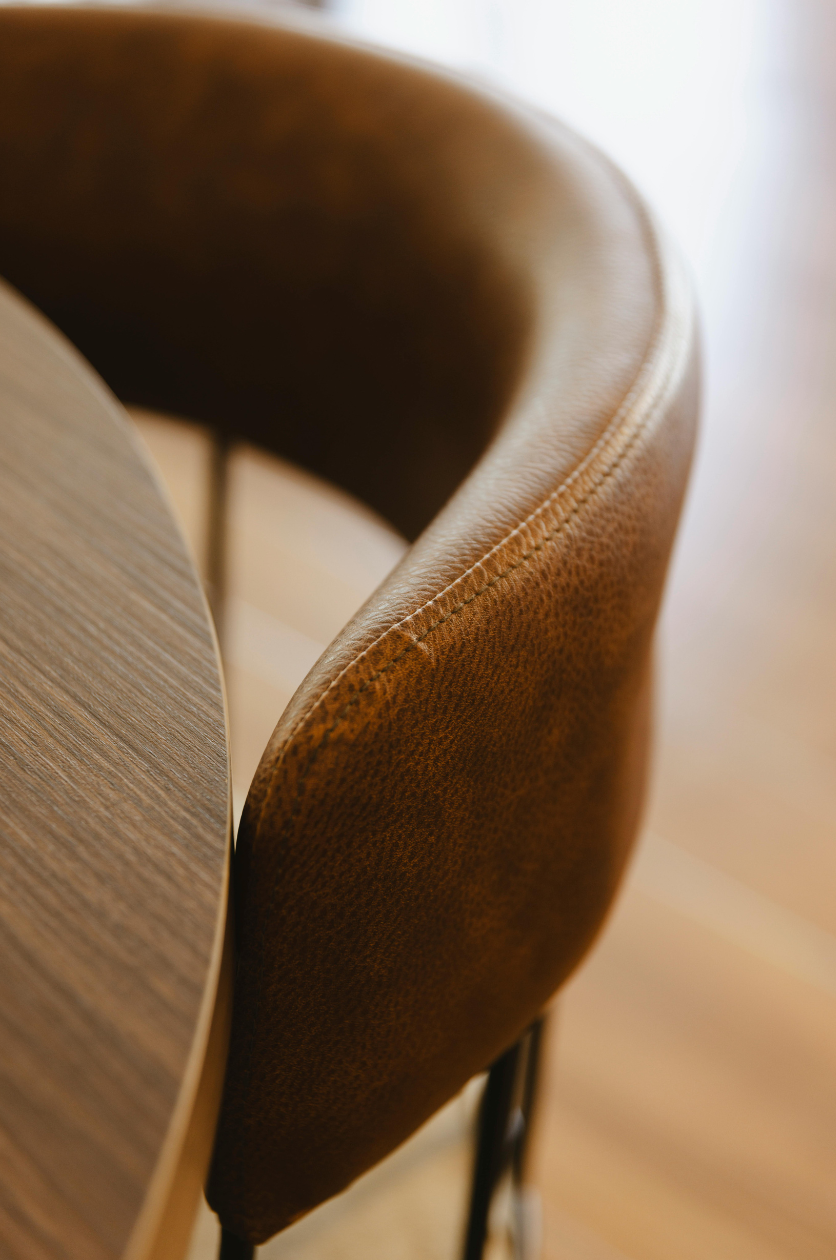 Close-up of a brown, textured leather chair positioned next to a round wooden table with a smooth surface.