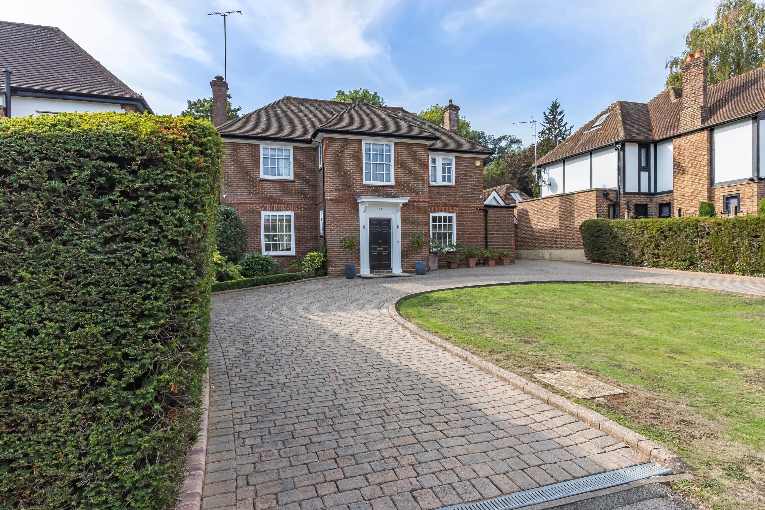Traditional brick houses surrounding a landscaped courtyard with cobblestone driveway, hedges, and manicured lawn