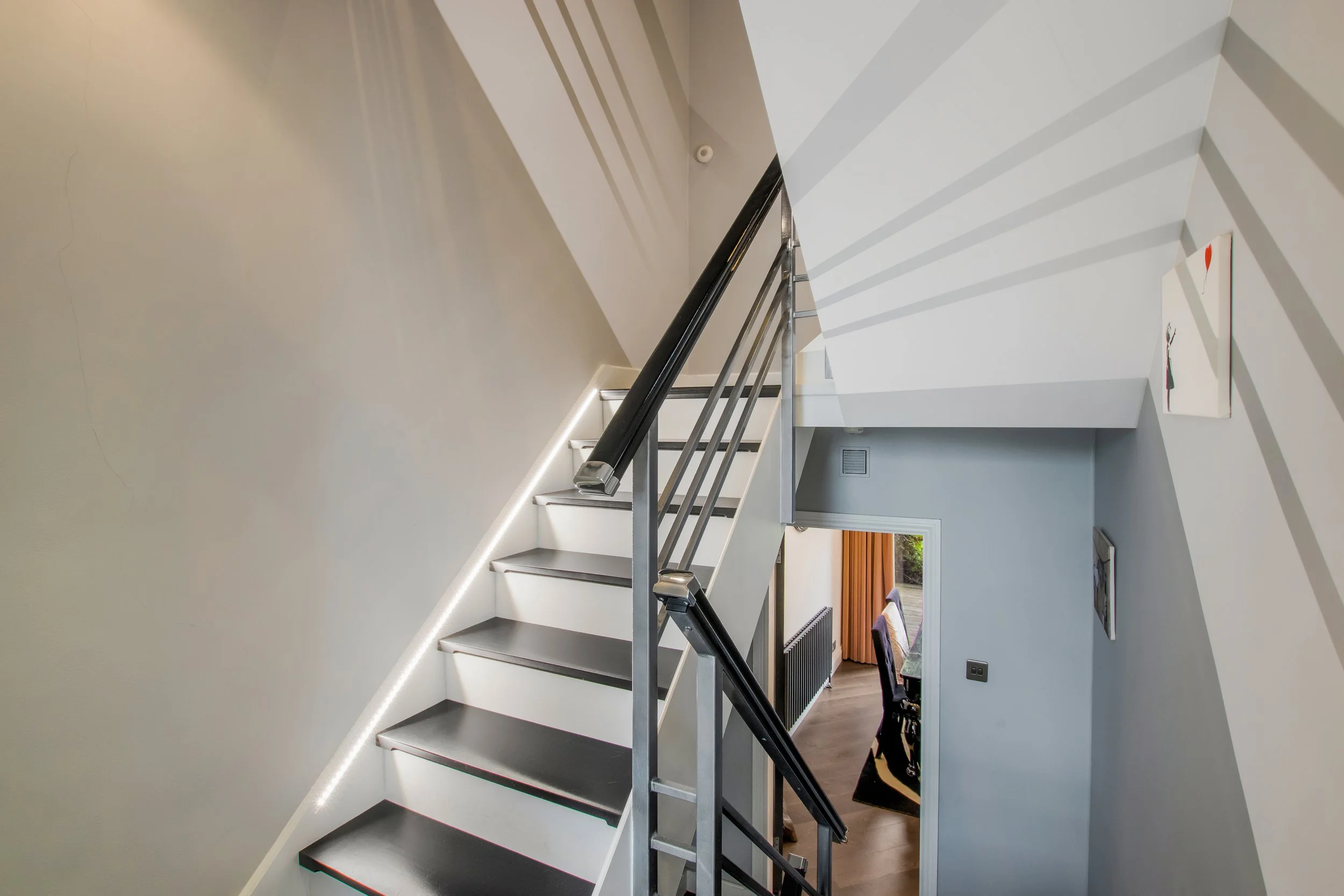 Modern indoor staircase with dark floating steps, black handrails, and metal railing in a contemporary home