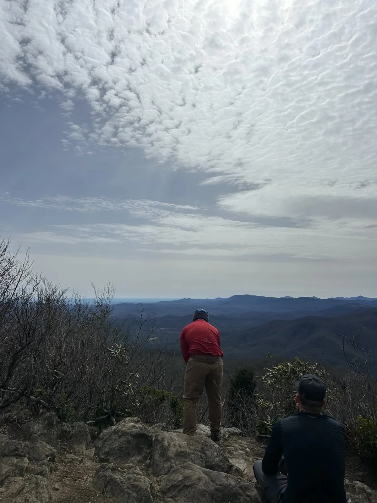 Two hikers overlooking a scenic mountain view with a cloudy sky.