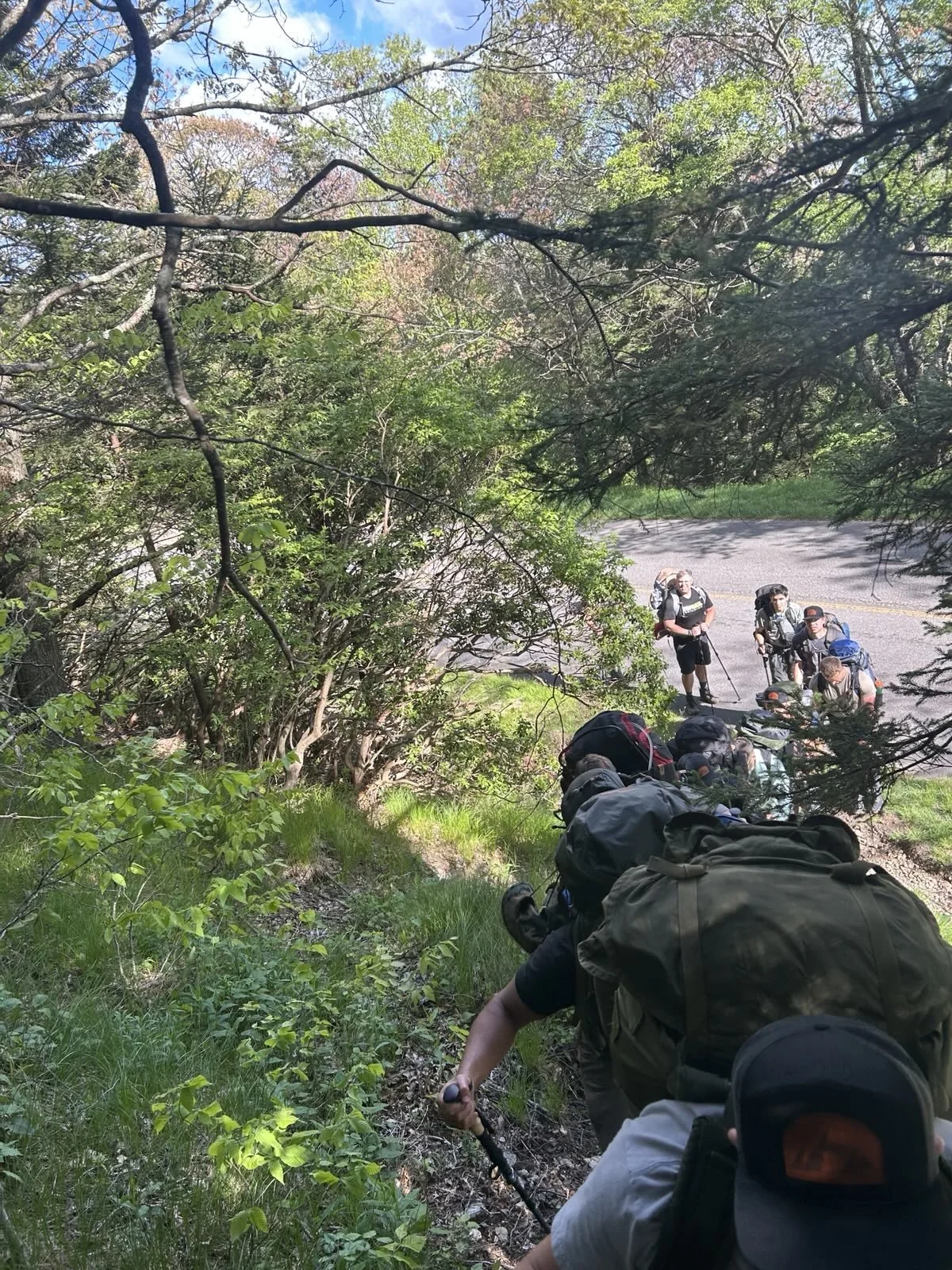 Group of hikers with backpacks walking along a wooded trail.