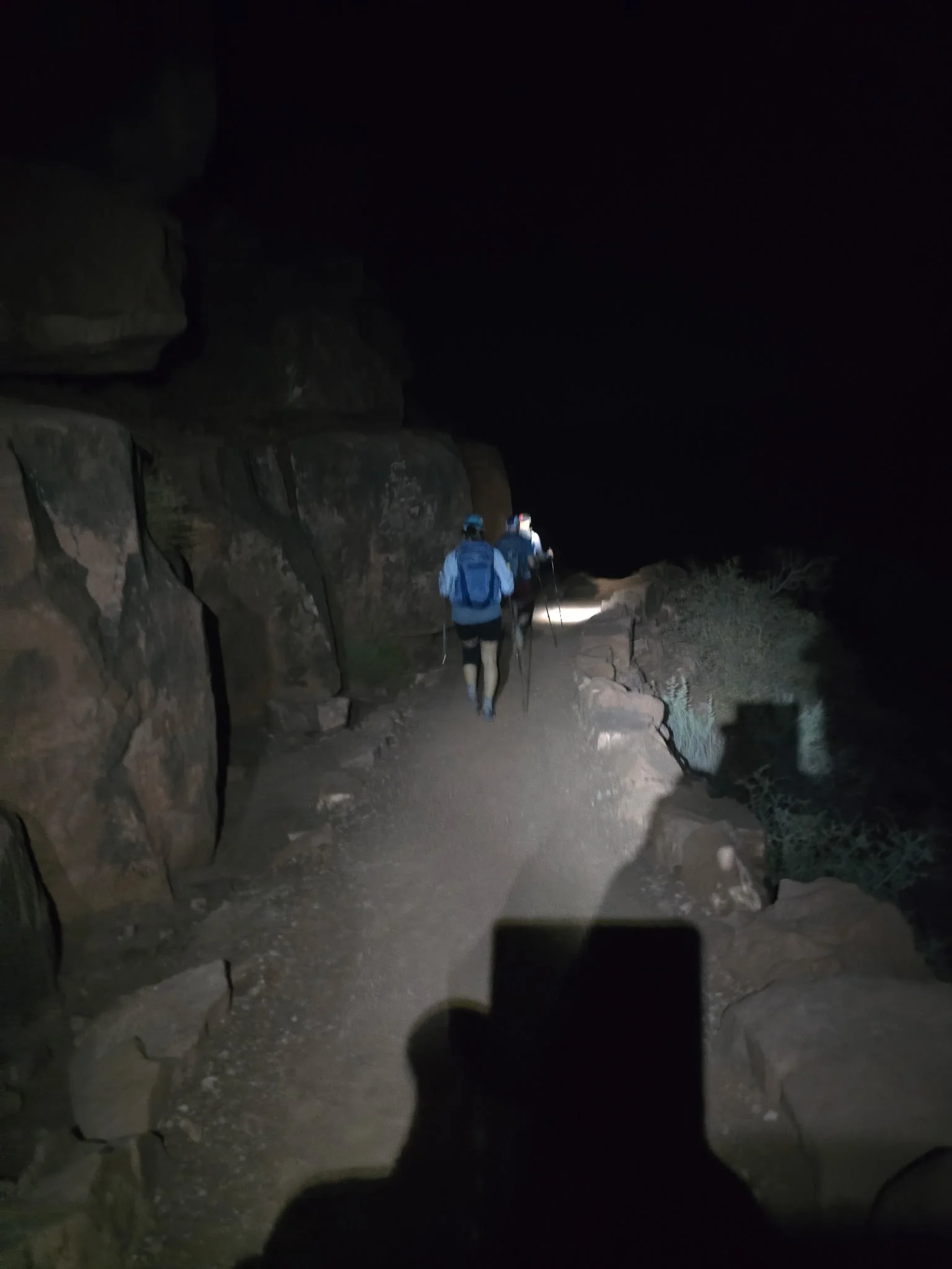Hikers walking on a rocky mountain trail at night with flashlights.