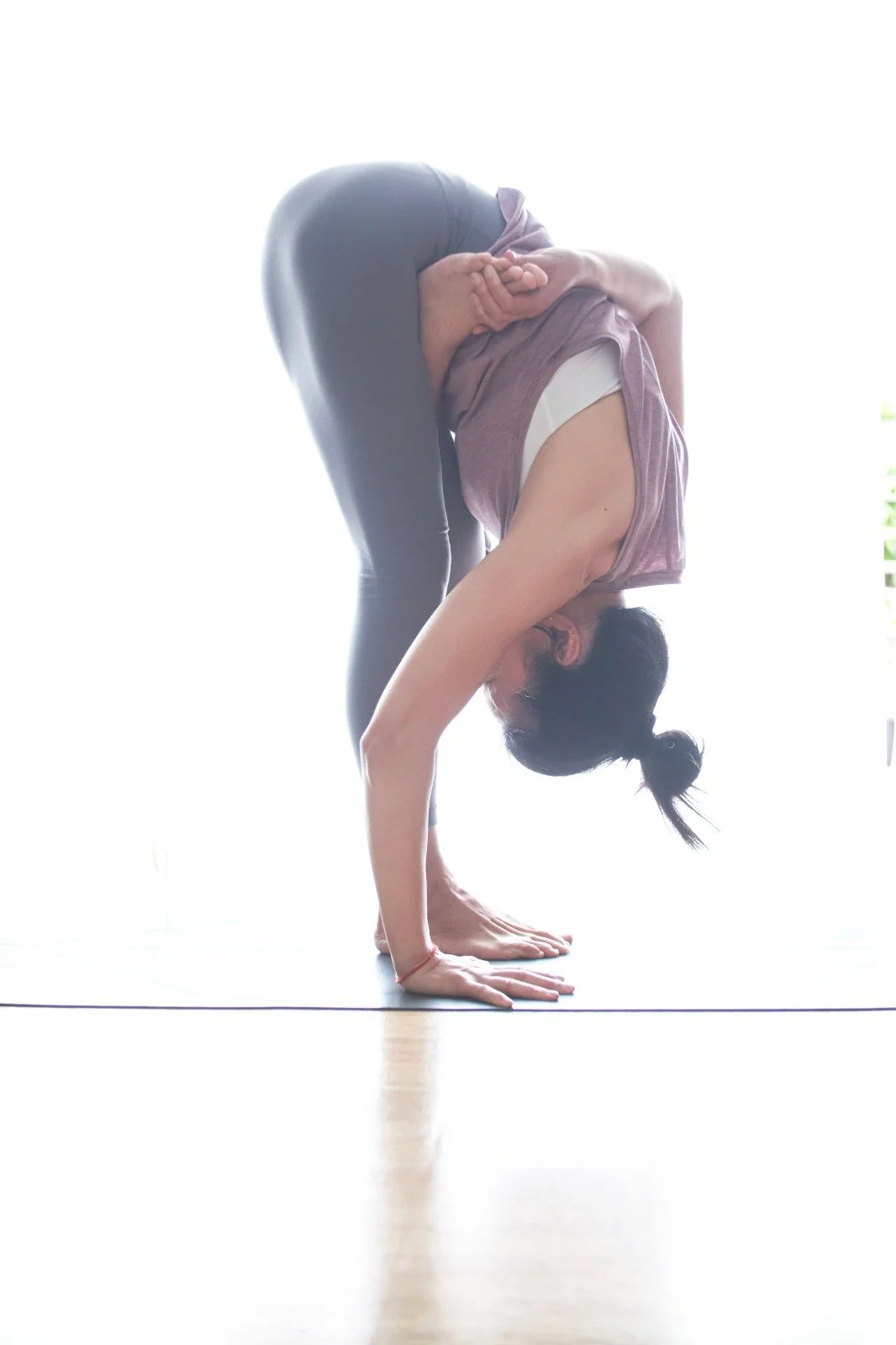 Mary Ma Yoga practicing yoga in a forward bend pose, with her hands on the floor and her head lowered between her knees.