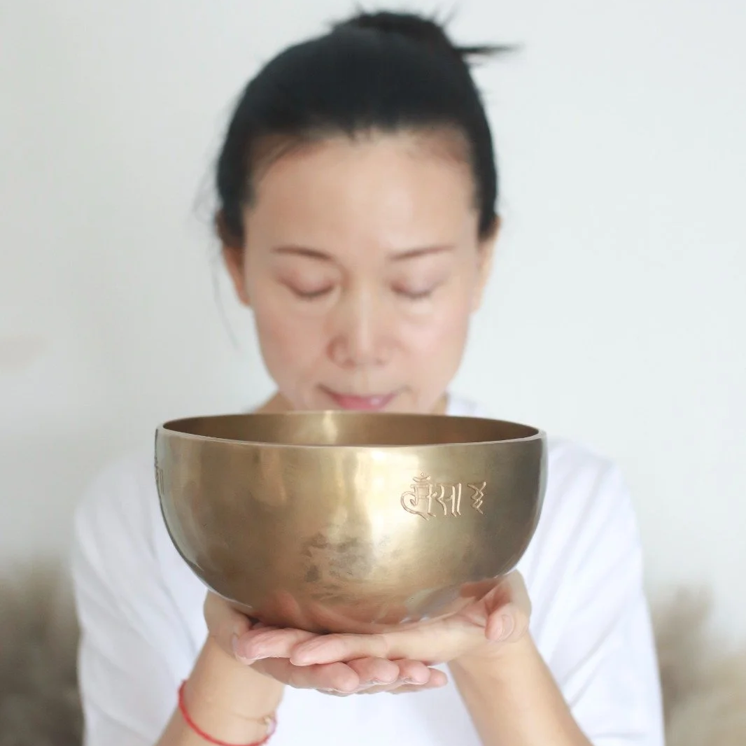 Mary Ma Yoga holding a brass singing bowl with Tibetan script engraved on it, eyes closed.
