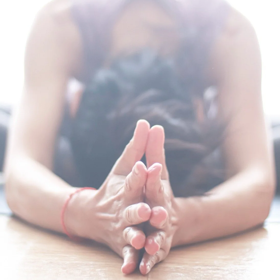 Mary Ma Yoga's hands pressed together in a prayer or yoga pose, resting on a wooden surface, with a blurred background.