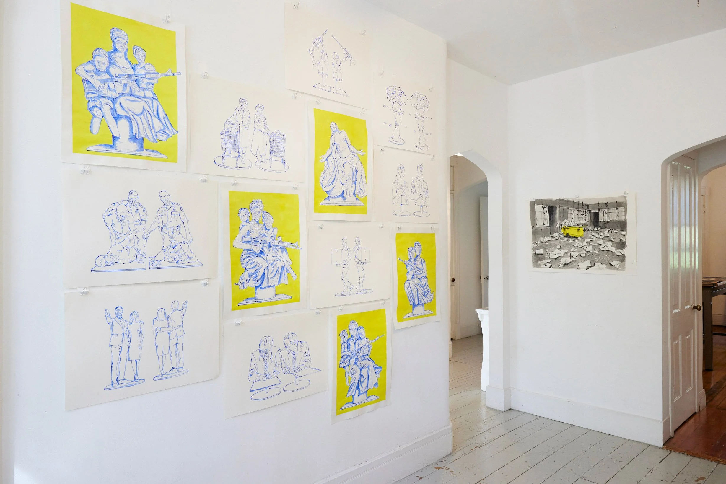 Gallery wall with sketches and colored illustrations of various people, some in historical clothing, on yellow backgrounds, arranged on a white wall; a framed black-and-white photo of a room with debris and a yellow container; a doorway leading to an