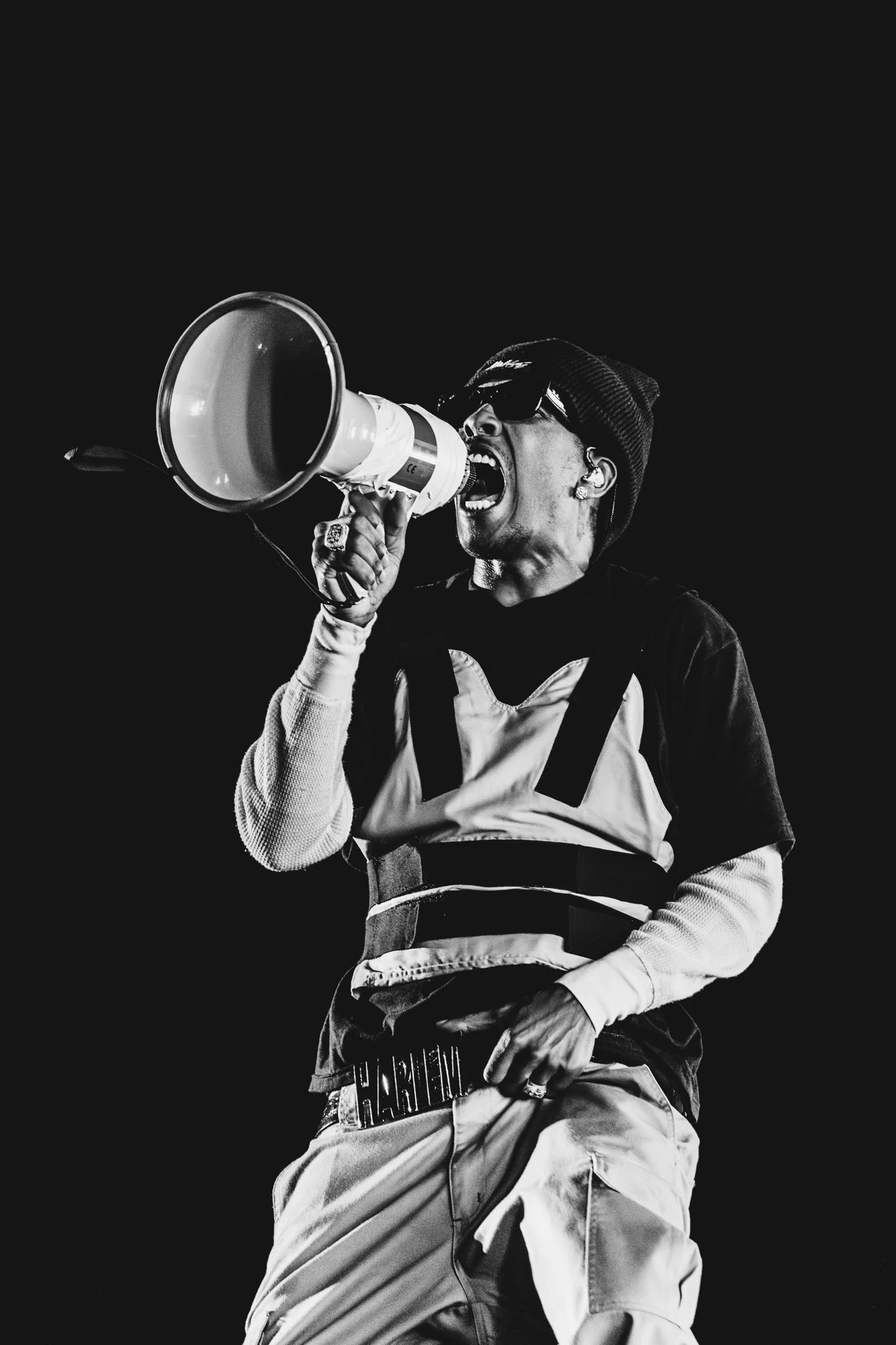 Artists ASAP Rocky at Festival Clout in Poland wearing sunglasses and a beanie passionately shouting into a megaphone.