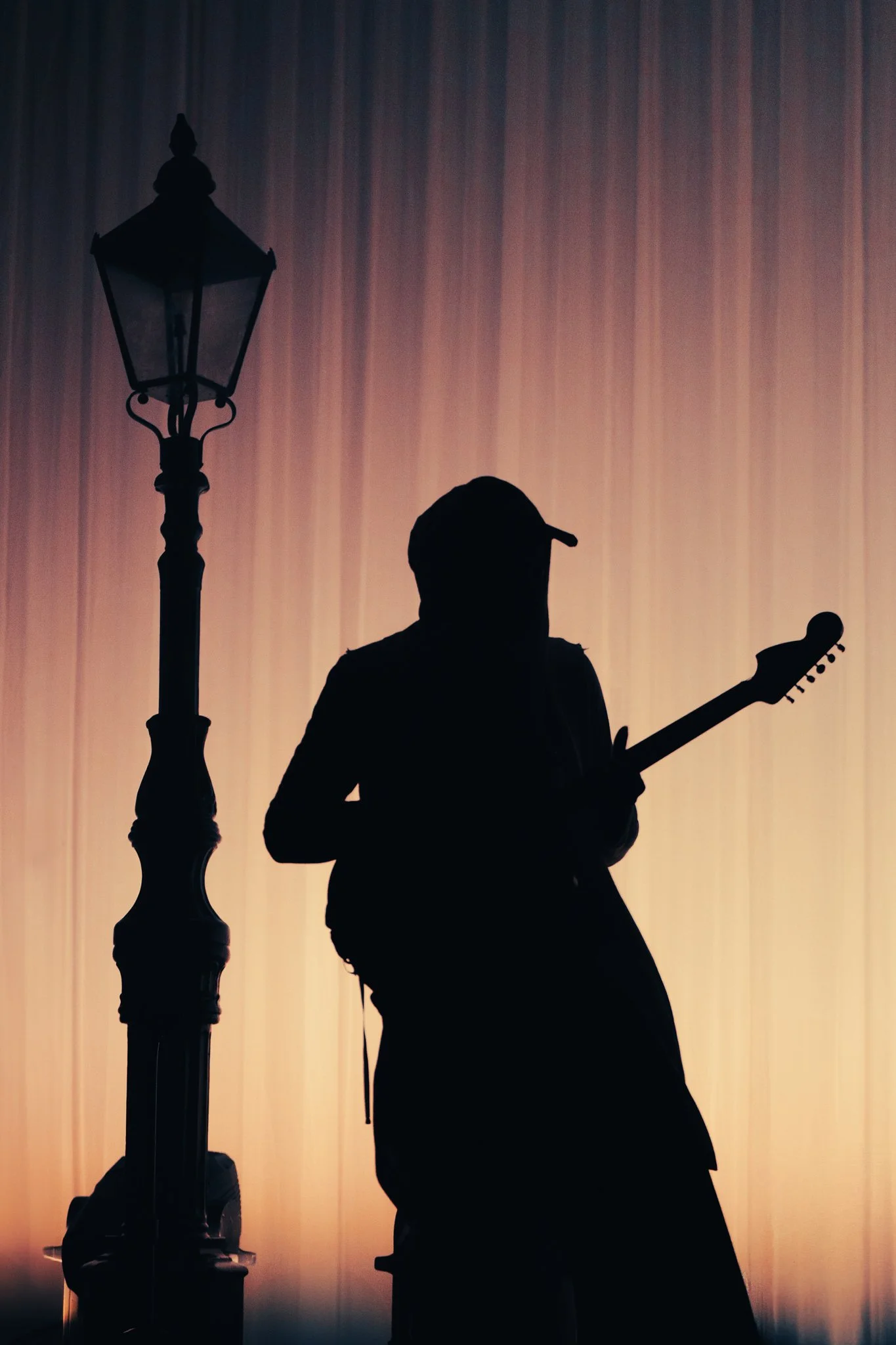 Silhouette of a Montell Fish in Amsterdam Melkweg playing guitar next to a street lamp at sunset