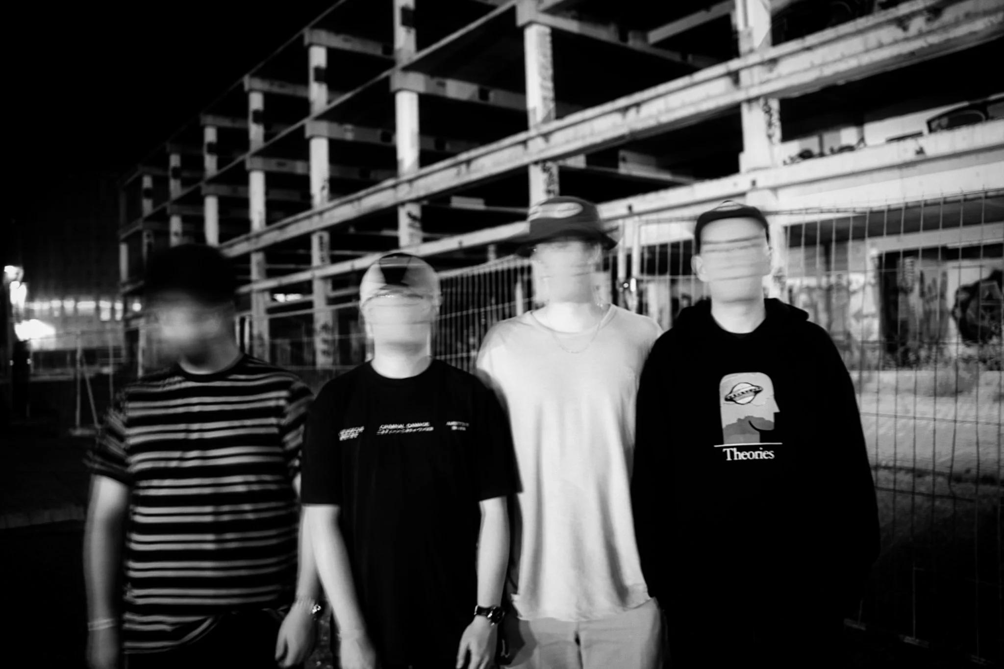 Four blurred young men standing against a construction site at night, with unfinished building and fencing visible in the background. Also the album cover for the UK band OMA.