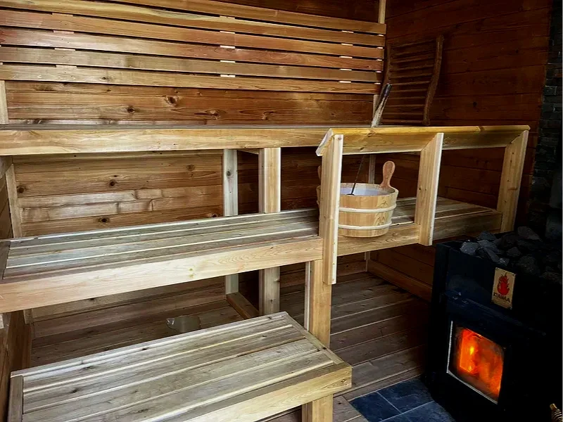 Indoor sauna with wooden benches, a bucket, and a ladle, near a stove with glowing heat.